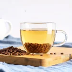 Benefits of cassia seed tea shown in a clear glass cup with roasted seeds on a wooden board