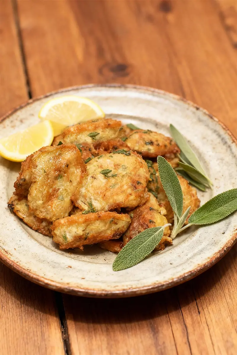 Classic Artichoke Francese: The Ultimate Guide to the Elegant Italian-American Dish 4 Artichoke Francese on a rustic plate with lemon wedges and sage.