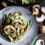 Creamy mushroom artichoke pasta piled on a rustic plate, topped with sautéed mushrooms and fresh sage.