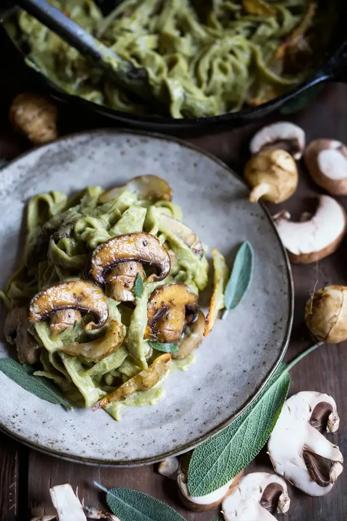 Creamy mushroom artichoke pasta piled on a rustic plate, topped with sautéed mushrooms and fresh sage.