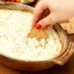 Best Gluten-Free Artichoke Dip Recipe: Creamy, Cheesy, and Perfect for Parties 5 Gluten-Free Artichoke Dip being scooped with a gluten-free cracker, surrounded by colorful vegetable sticks and crackers.
