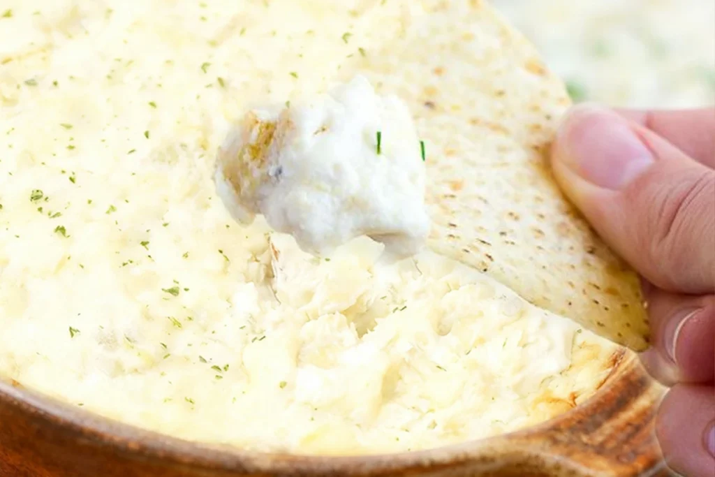 Best Gluten-Free Artichoke Dip Recipe: Creamy, Cheesy, and Perfect for Parties 7 Gluten-Free Artichoke Dip served on a gluten-free cracker chip, showing creamy texture and flecks of herbs.