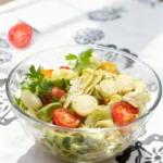 Artichoke and hearts of palm salad with cherry tomatoes and parsley, served in a clear glass bowl on a Mediterranean tablecloth.