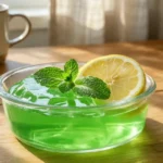 A gelatin weight loss recipe served in a glass bowl with a lemon slice and fresh mint on a wooden table.