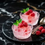 Dr. Oz pink gelatin recipe in glass bowls with fresh raspberries and mint on black marble surface