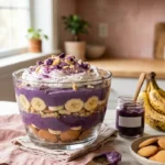 Ube banana pudding in a glass bowl showing distinct layers of purple ube custard, banana slices, vanilla wafers, and whipped cream topping.